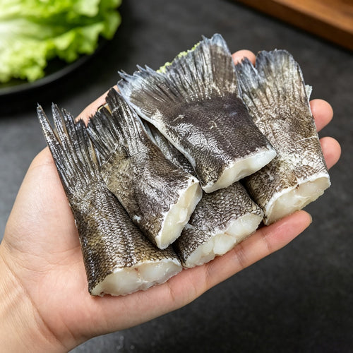 Raw skin-on cod tail portions held in one hand